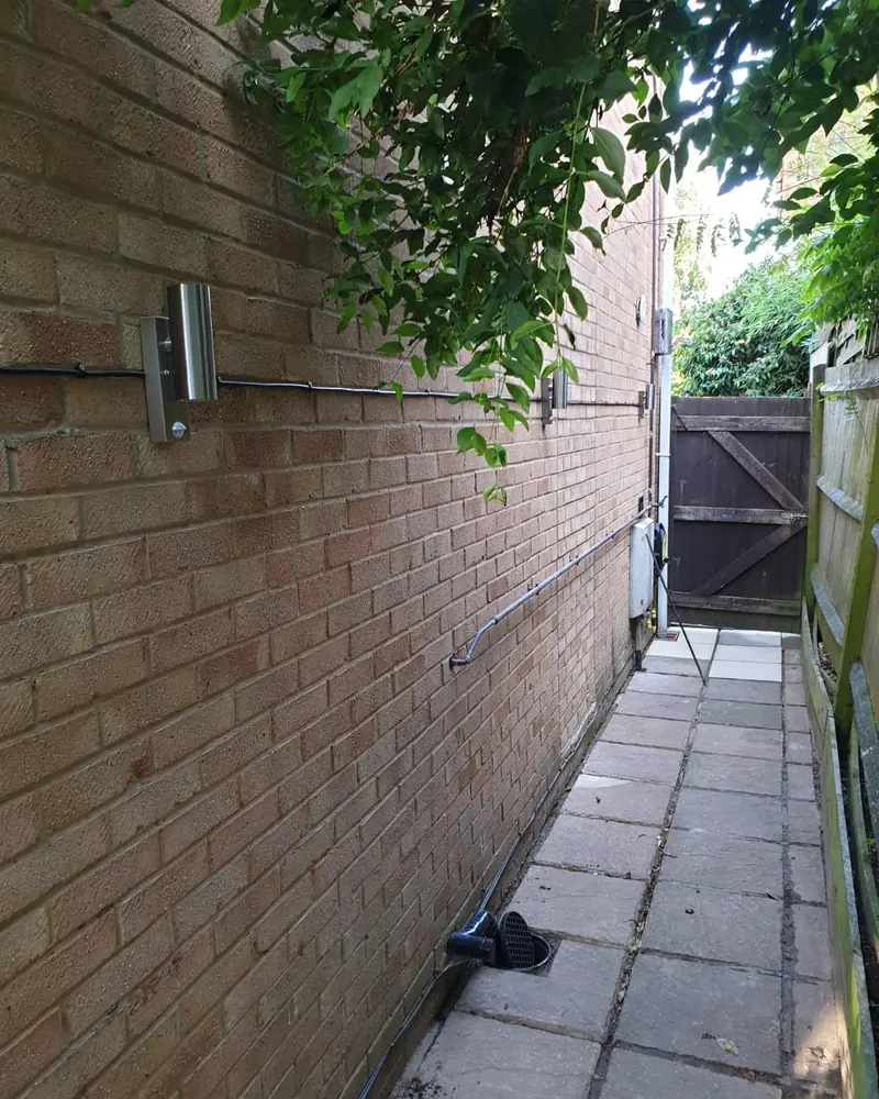 Stainless steel up-and-down wall lights fitted along the side path of a brick house