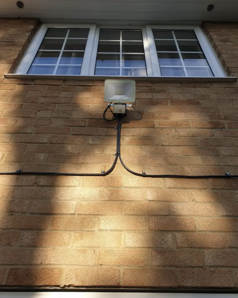 LED floodlight with a sensor fitted to a brick wall below a first-floor window